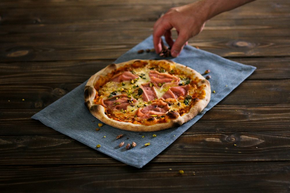 Gluten-free pizza base topped with ham and cheese on wooden table